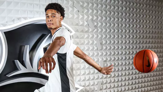 Men's basketball player Clyde Walters pointing at the camera and throwing a basketball behind the back