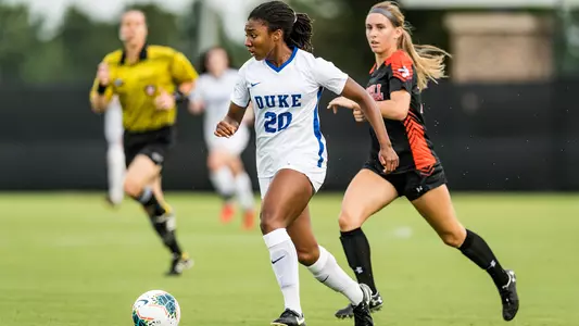 Women's Soccer player Mia Gyau kicking the ball in front of an opposing team player