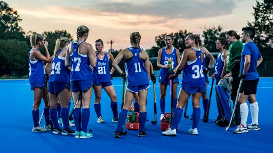 Duke field hockey team huddled up on blue turf under night clouds
