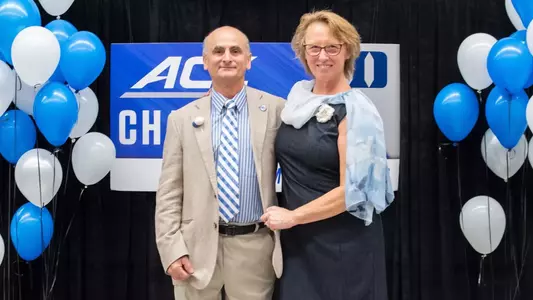 A photo of Alex and Elizabeth Beguinet standing together in front of the ACC Championship banner.