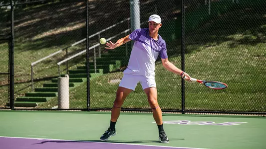 Maximus Dussault coils as he prepares to hit a forehand wearing a white and purple shirt.