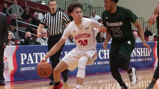 Javante McCoy holds the ball near the BU bench with a defender in front of him.