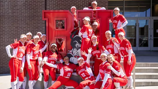 The BU softball team gathers for a group photo in front of the BU logo.