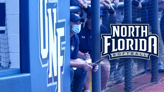 Picture of Marcie Higgs in the dugout at a softball game with the North Florida softball logo on the right side.