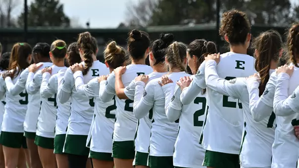 Members of the lacrosse team place their left hands on their teammate's shoulder during the playing of the national anthem