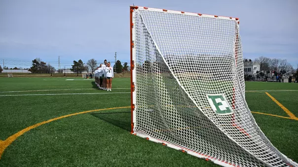 The lacrosse team stands in a single-file line facing the goal during the National Anthem
