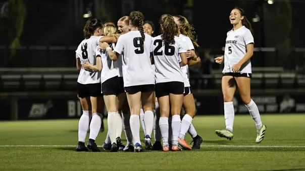 Women's soccer team huddle on Chapey Field at Anderson Stadium.