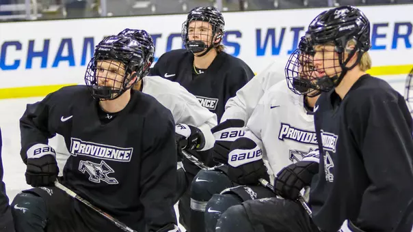 A picture featuring multiple men's hockey player listening to instructions on the ice at practice