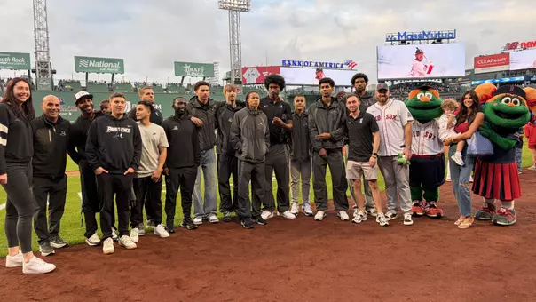 A group photo of the men's basketball team at the Friars at Fenway event on the Fenway Park field