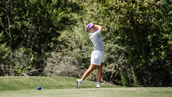 Claire Swathwood follows through on a tee shot with an iron while wearing a gray shirt