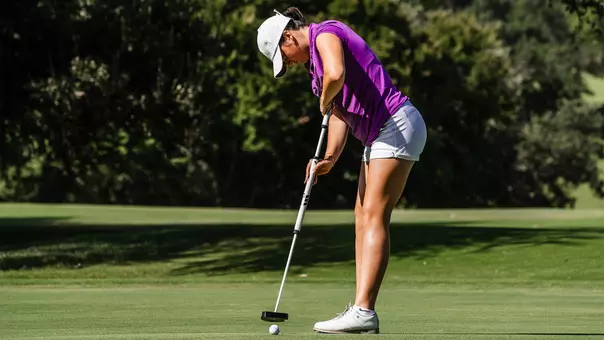 Gracie McGovern connects with a golf ball using a sweeper putter and wearing a magenta shirt
