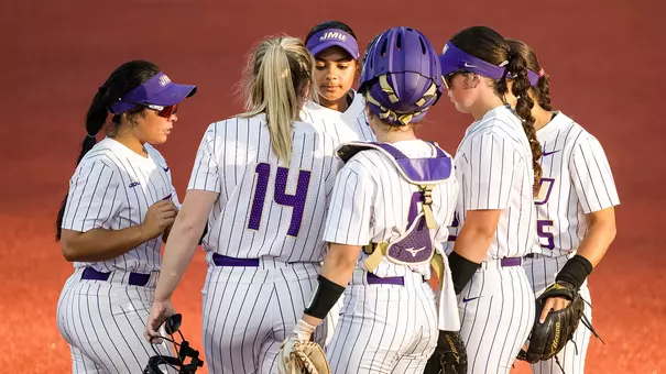 James Madison softball players have a group huddle mid game.