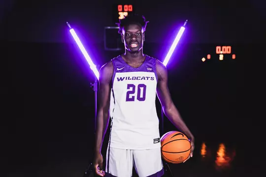 Ali Dibba poses with a basketball in front of bar lights on a basketball court