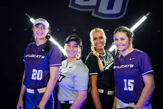 Wildcat softball pitchers smile at the camera in front of two bar lights