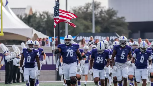 ACU football players run onto field carrying American Flag