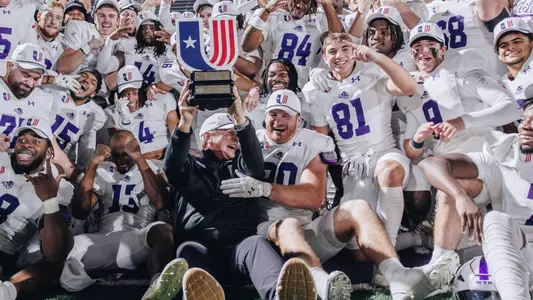 ACU Head football coach Keith Patterson holds the UAC championship trophy surrounded by players, including Kaghen Roach (90)