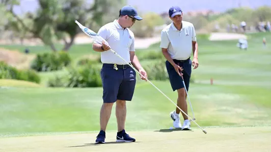Assistant Coach James Vargas pulls the flag for Johnny Walker to putt