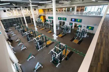 Interior photos of the Fudge Football Development Center weight room with racks of weights, dumbbells, squat racks, etc.