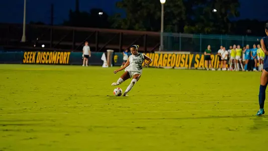 Baylor's Aryanna Jimison (No. 10) strikes a free kick during a night match against Marquette at Betty Lou Mays Field, with "Seek Discomfort" and "Courageously Sacri..." signage visible on the field wall behind her.