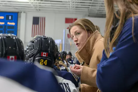 Kate Leary leans down on the bench while coaching at Merrimack.