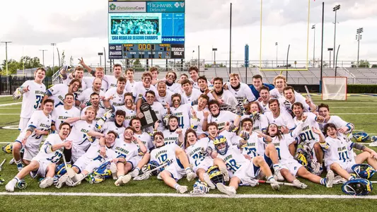 2021 men's lacrosse team poses with the regular season championship trophy after beating UMass