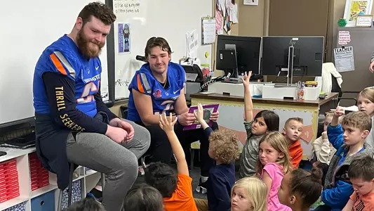 Boise State football players read to kids in an elementary classroom.