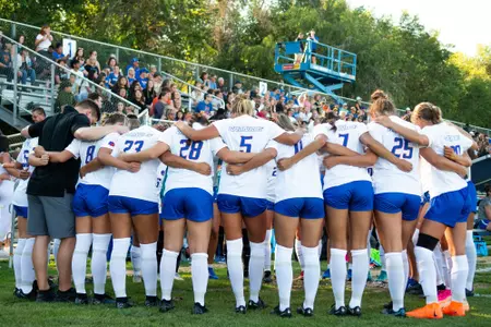 Photo of women's soccer team in a huddle before the start of the exhibition match, Aug. 11, 2023, against College of Idaho.