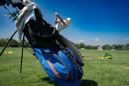 A Boise State golf bag with a golfer teeing off at the driving range on a blue sky day.