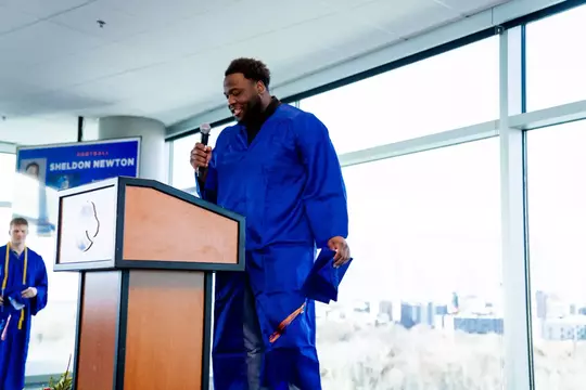 Sheldon Newton speaks at a podium in graduation gown.