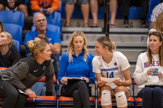 Annie Kaminski talking with coaches Hayley Peterson and Brindl Langley sitting on the bench during the Fresno State home match in 2023