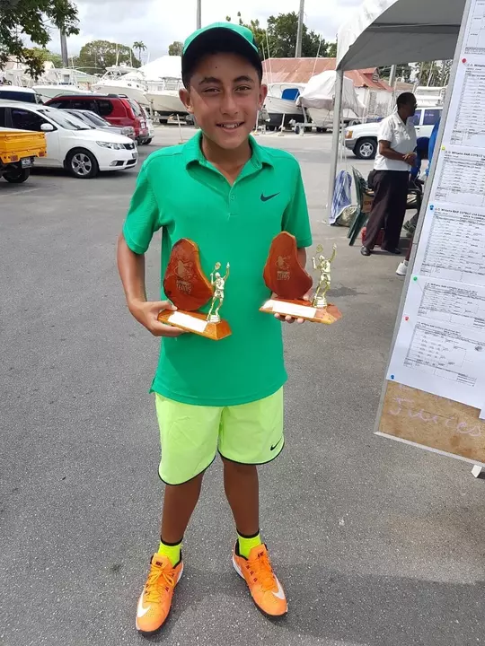 John Chin as a child holding two trophies and smiling.