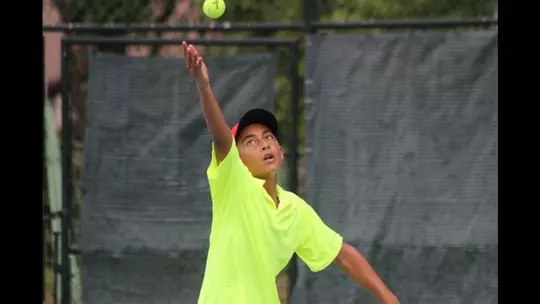 A young John Chin dressed in a bright yellow shirt serving during a match.