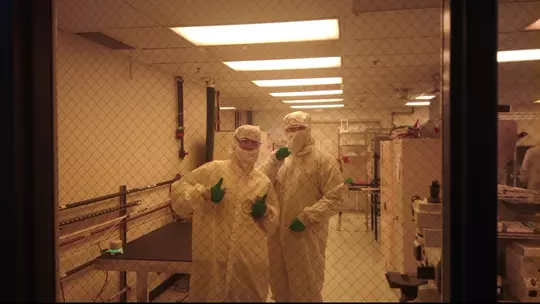 Elle Cotton poses with a classmate with both wearing in protective gear in a lab cleanroom.