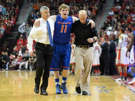 Tyler Smith assisting Leon Rice in helping an injured basketball player off the court