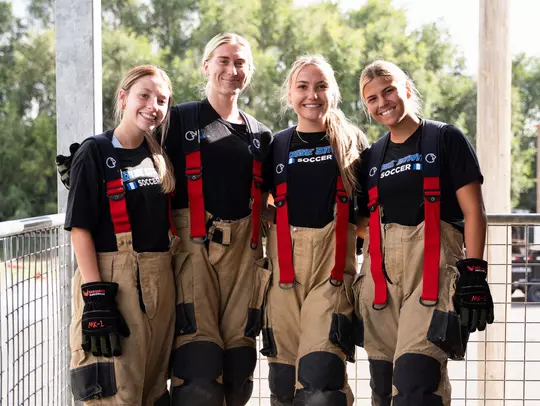 Alina Hernandez, Avery McBride, Tambree Bell and Kenzie MacMillan wearing fireman's gear pose for a shot while visiting a fire station in summer of 2025.