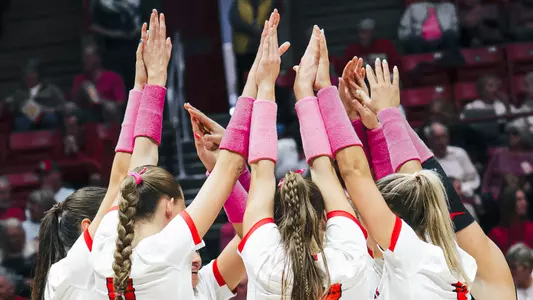 Women's volleyball team huddle with pink armbands for Dig Pink night in 2025