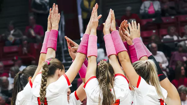 Women's volleyball team huddle with pink armbands for Dig Pink night in 2025