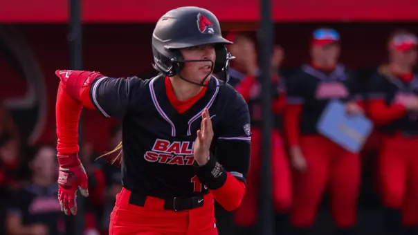 Paige Kelley running to first base in her black top and red pants after a hit at the Ball State Softball Stadium