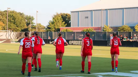 Soccer team in red uniforms runs on the field during Thursday night's match at Purdue
