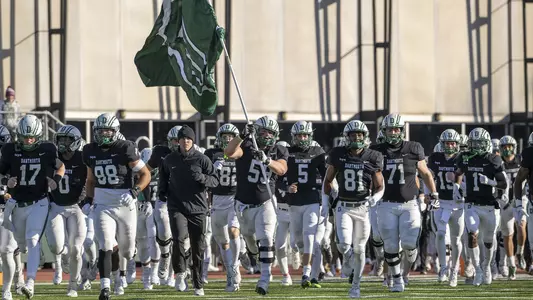 Team running with flag prior to football action versus Brown