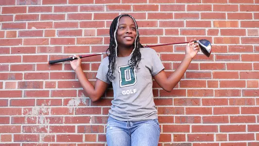 Hope Hall against a brick wall with golf club behind her head