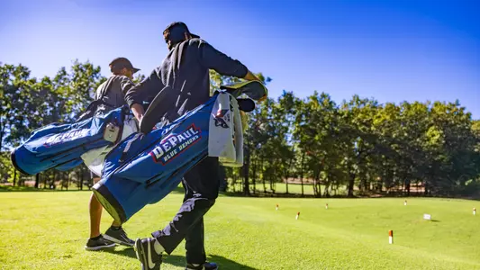 two golfers walking on course with blue golf bag that says "DePaul Blue Demons" in focus