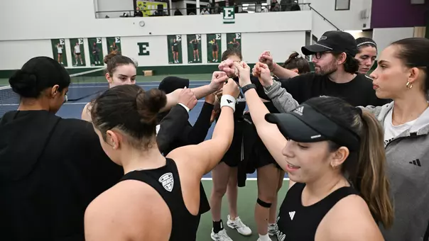 The tennis team huddles with one hand in the center before taking the courts against Oakland
