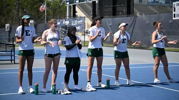 Players from the Eastern Michigan tennis team line the court and cheer on a teammate in the final match at North Florida