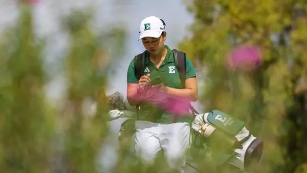 Baiyok Sukterm, with flowers in the foreground, looks over her scorecard as she walks down the fairway toward her ball for her second shot