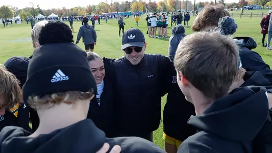 Cross Country Coaches Austin Whitelaw and Jenna Zydanowicz smile in the men's team huddle at 2025 Cross Country Championships