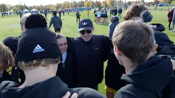 Cross Country Coaches Austin Whitelaw and Jenna Zydanowicz smile in the men's team huddle at 2025 Cross Country Championships