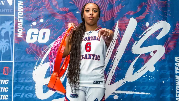 Florida Atlantic WBB Signee - Jazzy Gipson posing with a basketball net on her right side and pointing at the camera with her right hand