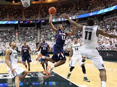 Mar 1, 2014; East Lansing, MI, USA; Illinois Fighting Illini guard Tracy Abrams (13) drives to the basket against Michigan State Spartans guard Keith Appling (11) and guard Denzel Valentine (45) during the 2nd half of a game at Jack Breslin Student Events Center. Illinois won 53-46. Mandatory Credit: Mike Carter-USA TODAY Sports