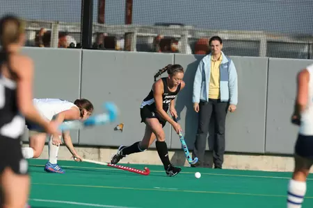 Field Hockey midfielder Salene Shaffer dribbles the ball out of the opposing circle while a defender trails closely behind.